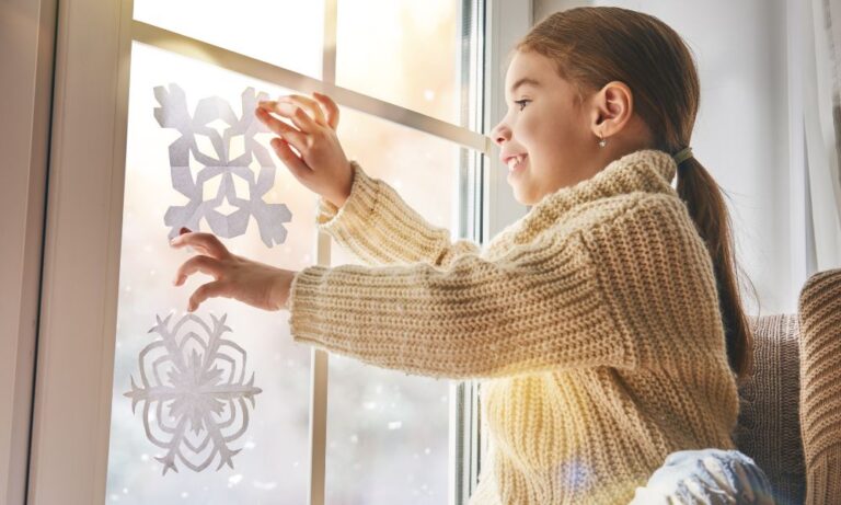 girl placing paper snowflakes on the window of her Houston home